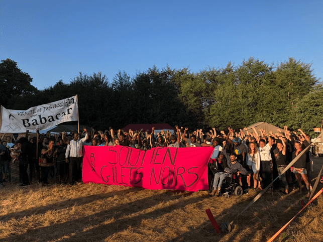 A big group of people holding posters and banners. In the background tall trees are visible.